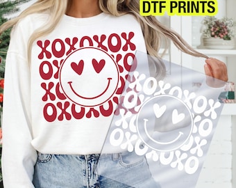 Puede incluir: Sudadera blanca con diseño rojo de XOXO y carita sonriente. La carita sonriente tiene ojos en forma de corazón. Las palabras "READY TO PRESS DTF PRINTS" están en un cuadro amarillo en la esquina superior derecha.