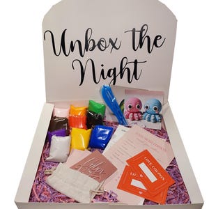 May include: A white gift box with the text "Unbox the Night" contains various items. Inside are colorful packages, a blue toy, two octopus figurines, cards, and orange "Love Coupon" cards. The box is filled with pink shredded paper.
