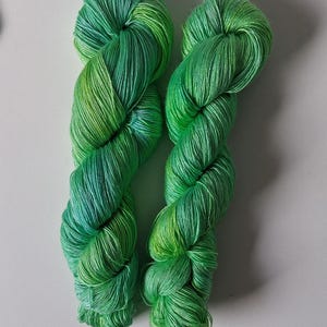 Peut inclure: Deux &eacute;cheveaux de fil vert vif avec un effet d&eacute;grad&eacute;, passant du vert jaune clair &agrave; un vert plus profond et plus riche. Le fil est &eacute;troitement enroul&eacute;, mettant en valeur sa texture et ses variations de couleur. Id&eacute;al pour les projets de tricot ou de crochet.