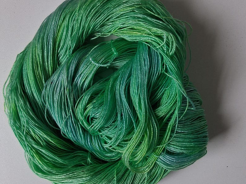 Peut inclure: Une pelote de fil vert avec des nuances de vert et de bleu. Le fil est &eacute;troitement enroul&eacute;, cr&eacute;ant un aspect dense et textur&eacute;. La couleur passe du vert clair au vert fonc&eacute;.
