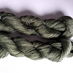 May include: Two skeins of olive green yarn are shown against a white backdrop. The yarn is tightly twisted, with a subtle sheen. The texture suggests a soft, natural fibre, suitable for knitting or crochet projects.