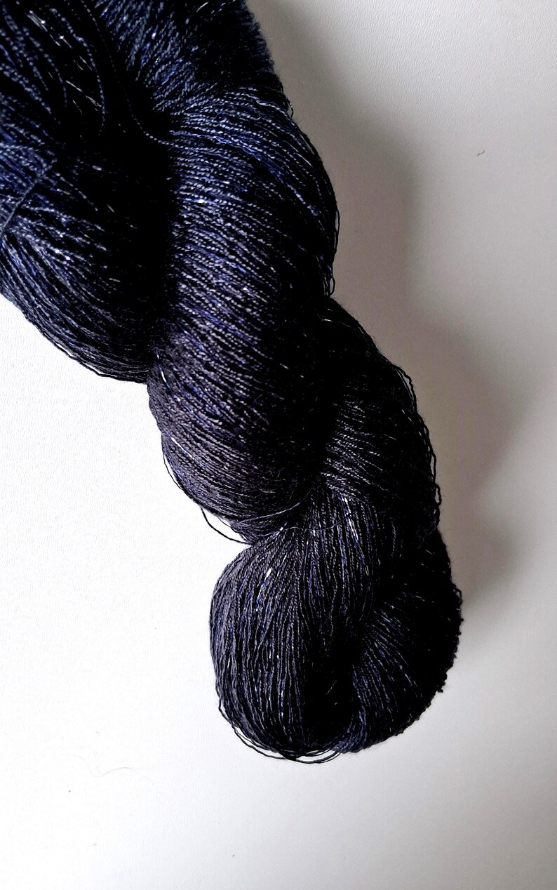 K&ouml;nnte beinhalten: Ein Strang dunkelmarinefarbenes Garn mit dezentem Glanz. Das Garn scheint eng gesponnen zu sein, mit einer leicht strukturierten Oberfl&auml;che. Die Farbe ist ein tiefes, sattes Blau mit silbernen Akzenten. Ideal f&uuml;r Strick- oder H&auml;kelprojekte.