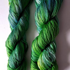 May include: Two skeins of vibrant green yarn with subtle blue and yellow highlights. The yarn is tightly twisted, creating a textured appearance. The color gradient adds depth and visual interest, perfect for knitting or crochet projects.