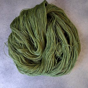 May include: A skein of olive green yarn, tightly wound and textured. The yarn appears to be made of many fine strands, creating a soft, yet defined, appearance. The yarn is suitable for knitting, crocheting, or other fiber arts projects.