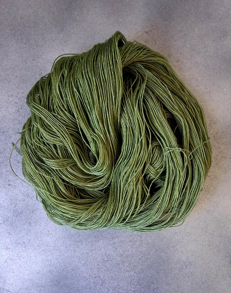 May include: A skein of olive green yarn, tightly wound and textured. The yarn appears to be made of many fine strands, creating a soft, yet defined, appearance. The yarn is suitable for knitting, crocheting, or other fiber arts projects.