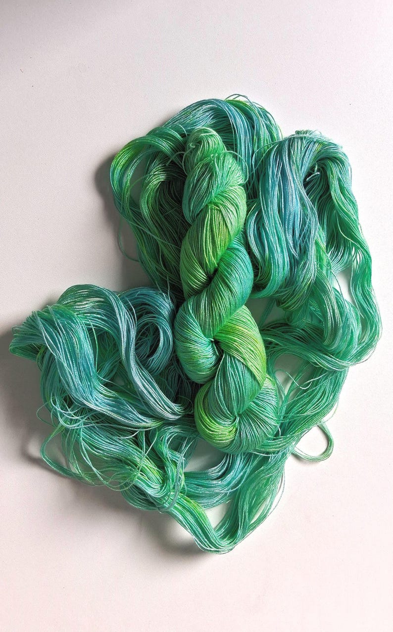 Peut inclure: Une &eacute;cheveau de fil teint &agrave; la main dans des tons de vert et de sarcelle. Le fil est d'un poids fin et doux, parfait pour les projets de tricot ou de crochet. Les couleurs se m&eacute;langent, cr&eacute;ant un effet de d&eacute;grad&eacute;.