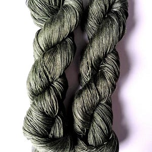 May include: Two skeins of olive green yarn are shown against a white backdrop. The yarn is tightly twisted, with a subtle sheen. The colour is a muted, earthy green, suitable for knitting or crochet projects.