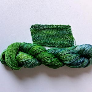 May include: A skein of vibrant green yarn with shades of blue and white, next to a small knitted swatch. The yarn is tightly twisted, showcasing a gradient of colors. The knitted swatch displays the same color variations.