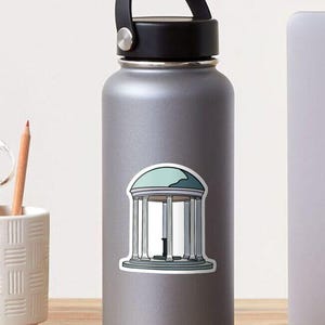 May include: A sticker featuring a teal and white illustration of a classical rotunda with columns and a domed roof. The sticker is applied to a gray water bottle with a black handle.