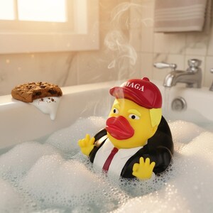 May include: A yellow rubber duck wearing a red cap with the text MAGA, a black suit jacket, a white shirt, and a red tie. The duck has blonde hair, red lips, and is positioned in a bathtub filled with white soap bubbles, with steam rising above.