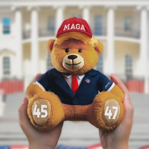 May include: A plush teddy bear wearing a red "MAGA" hat, a blue suit, and a red tie. The bear has blonde hair and the numbers "45" and "47" are printed on its paws. The bear is a political novelty item.