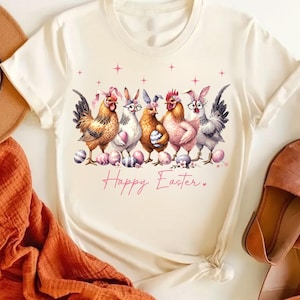 May include: A white t-shirt with a graphic of five chickens wearing bunny ears and glasses. The chickens are holding Easter eggs and the text "Happy Easter" is written below them.