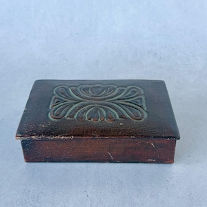 May include: A white ceramic mug with a black handle and the text "But First, Coffee" in a bold, black font. The mug is set against a blurred background, suggesting a cozy setting.