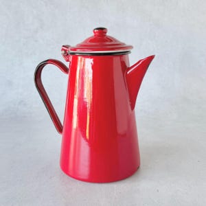 May include: A vibrant red enamelware coffee pot with a black handle and spout. The pot has a matching lid with a black knob and a white trim. This vintage-style coffee pot is perfect for brewing coffee.