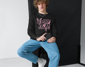 May include: Black long-sleeve shirt with the text "Good Life" in a pink, retro font. The shirt is paired with light blue jeans. The person is holding a black phone.