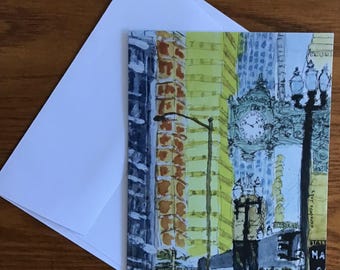 May include: A watercolor painting of a city street scene with tall buildings, a clock tower, and a street lamp. The buildings are painted in shades of blue, yellow, and orange. The clock tower is painted in a light blue and white color scheme. The street lamp is painted in a dark brown color. The painting is signed "Stephen Wagner" in the lower right corner.