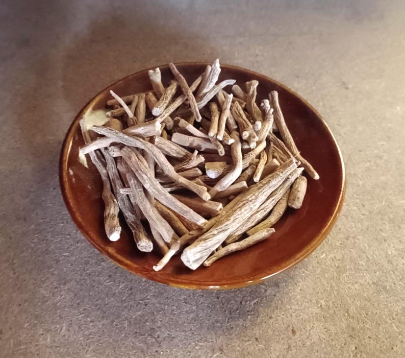 May include: A brown ceramic bowl filled with dried, light brown, and beige root pieces. The roots are of varying lengths and thicknesses, with a slightly rough texture. The bowl is round with a dark brown rim.