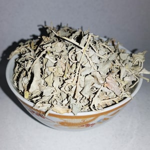 May include: A white ceramic bowl filled with dried, light brown, and gray herbs. The bowl has a decorative pattern of orange and red flowers.