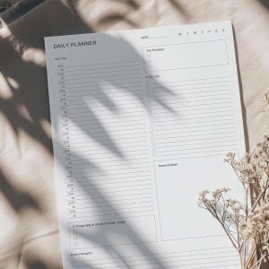 May include: A white daily planner with a black header that says "Daily Planner". The planner has sections for "Your Day", "Top Priorities", "To-Do List", "Notes & Ideas", "3 Things (Big or Small) to Finish Today", and "Extra Thoughts".