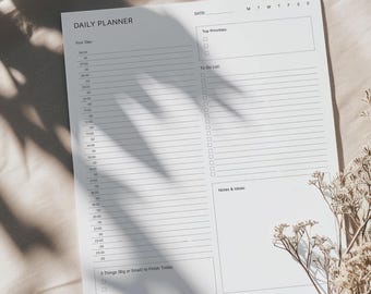 May include: A white daily planner with a black header that says "Daily Planner". The planner has sections for "Your Day", "Top Priorities", "To-Do List", "Notes & Ideas", "3 Things (Big or Small) to Finish Today", and "Extra Thoughts".