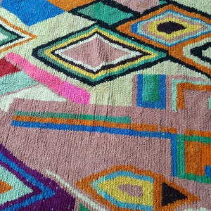 May include: A colorful, geometric rug with a textured surface. The rug features a variety of shapes, including diamonds, squares, and triangles, in shades of pink, blue, green, orange, and yellow. The rug's design is a mix of abstract and traditional patterns.
