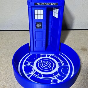 Puede incluir: Modelo azul impreso en 3D de una cabina de polic&iacute;a, con el texto "POLICE PUBLIC BOX" en la parte superior. Tiene una base circular con un dise&ntilde;o geom&eacute;trico blanco. La puerta est&aacute; abierta, revelando el interior.