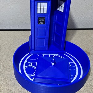 Puede incluir: Un modelo azul impreso en 3D de la ic&oacute;nica cabina de polic&iacute;a brit&aacute;nica, la TARDIS, de la serie Doctor Who. El modelo presenta el texto "POLICE PUBLIC CALL BOX" en la parte superior y est&aacute; sobre una base circular con detalles blancos.