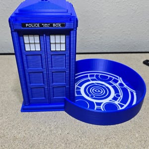 Puede incluir: Una cabina de polic&iacute;a azul impresa en 3D con una bandeja circular adjunta. La caja tiene las palabras "POLICE PUBLIC BOX" en la parte superior. La bandeja tiene un dise&ntilde;o circular blanco.