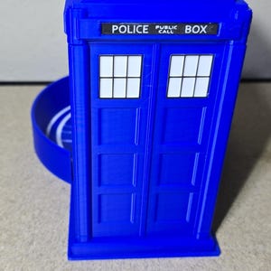 Puede incluir: Una r&eacute;plica azul de una cabina de polic&iacute;a con las palabras "POLICE PUBLIC CALL BOX". Tiene dos ventanas con marcos blancos y una peque&ntilde;a luz. El dise&ntilde;o es similar a una cabina telef&oacute;nica brit&aacute;nica.