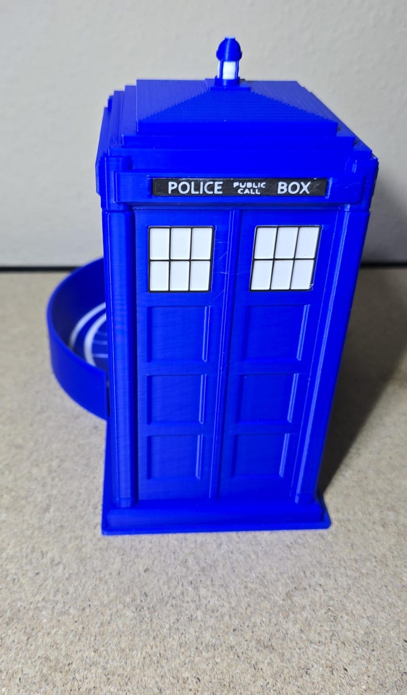 Puede incluir: Una r&eacute;plica azul de una cabina de polic&iacute;a con las palabras "POLICE PUBLIC CALL BOX". Tiene dos ventanas con marcos blancos y una peque&ntilde;a luz. El dise&ntilde;o es similar a una cabina telef&oacute;nica brit&aacute;nica.