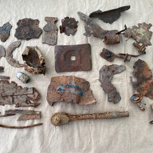 May include: A collection of assorted rusted metal fragments, including flat plates, a wrench, a coiled spring, bolts, and irregular scrap pieces. The items exhibit heavy oxidation, varying textures, and brown, orange, and grey metallic tones.