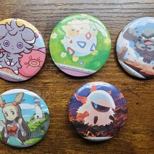 May include: Five colorful round pinback buttons featuring various Pokémon characters. Each button has a unique design, including illustrations of Togepi, Golem, and other characters. The buttons are set against a wooden background.