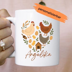 Könnte beinhalten: Weiße Keramik-Tasse mit einem herzförmigen Design mit Hühnern, Küken, Eiern und einem kleinen Stall. Der Name "Angelika" ist in einer Schriftart geschrieben. Ein orangefarbenes Banner mit dem Text "personalisierbar" ist sichtbar.