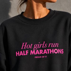 Può includere: Una felpa nera a girocollo con il testo rosa "Hot girls run HALF MARATHONS PROUD OF IT" stampato sul davanti. Il capo presenta uno scollo a coste e maniche lunghe, mettendo in mostra un audace design grafico con un mix di caratteri corsivi e stampatello.
