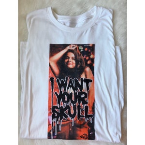 May include: White t-shirt with a graphic print of a woman with the text "I WANT YOUR SKULL" in black dripping paint.
