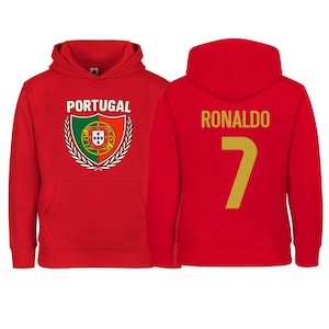 May include: Red hooded sweatshirt. The front features the word "PORTUGAL" above a crest with the Portuguese flag and a laurel wreath. The back displays "RONALDO" and the number "7" in gold.
