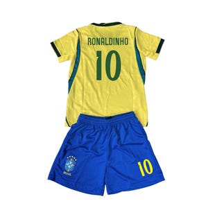 May include: A yellow and blue soccer uniform set. The jersey has the name "RONALDINHO" and the number "10" on the back. The shorts are blue with the number "10" and a team emblem. The uniform is likely for a youth.