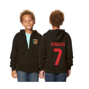 May include: Black zip-up hoodie with the name "RONALDO" and the number "7" in red on the back. The front features a "PORTUGAL" patch with a crest. The hoodie is worn by a person.