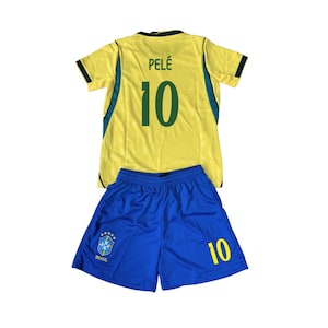 Puede incluir: Un conjunto de camiseta de fútbol amarilla y verde y pantalón corto azul. La camiseta tiene el nombre "PELÉ" y el número "10" en la espalda. El pantalón corto tiene el número "10" en la pierna y un emblema "BRASIL".