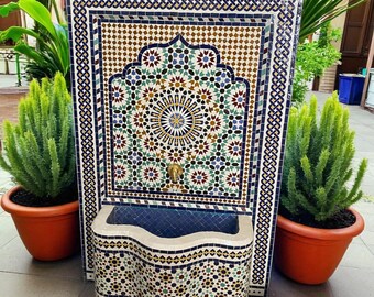 May include: A decorative mosaic fountain with a central floral design, surrounded by geometric patterns in shades of blue, green, brown, and white. The fountain has a curved basin and is flanked by potted plants in terracotta pots.