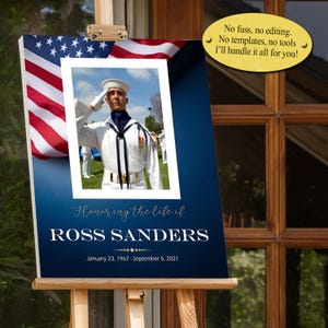 Può includere: Un cartello commemorativo con una foto di un uomo in uniforme della marina che saluta, su sfondo blu con una bandiera americana. Il testo recita "Honoring the life of ROSS SANDERS" con le date. Il cartello è su un cavalletto di legno.