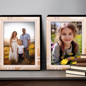 May include: Two framed photos, one with a family of three standing in a field, and the other with a young girl smiling in a field of flowers. The frames are black with a white and peach border.