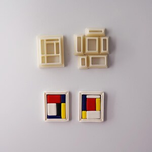 May include: Four cookie cutters and two finished cookies. The cookie cutters are beige and in the shape of rectangular frames and geometric shapes. The finished cookies are in white frames with red, blue, yellow, and white geometric designs.