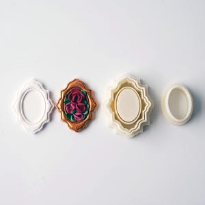 May include: Four white and gold plastic cookie cutters in the shape of an oval frame. The center cutter has a floral design with pink and green details.