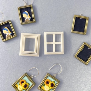 May include: Earrings featuring miniature framed art, including a sunflower design and a depiction of the "Girl with a Pearl Earring." Additional frames and window-shaped craft supplies are also present, all set against a light gray background.