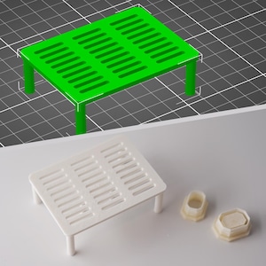 Puede incluir: Un soporte de plástico blanco con un patrón de rejilla en la parte superior. El soporte tiene cuatro patas y mide aproximadamente 15 cm de largo y 10 cm de ancho.