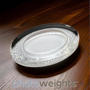 May include: Oval-shaped clear glass dish with a white interior. The rim features a textured, patterned design. The dish sits on a dark wooden surface, with the word "photoweights" visible in the bottom right corner.