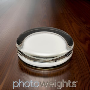 May include: A clear glass paperweight with a rounded shape. The paperweight is sitting on a wooden surface.