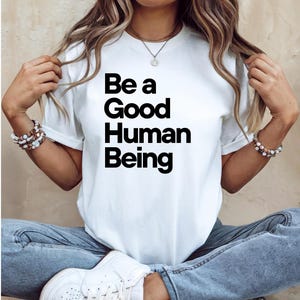 May include: White t-shirt with black text that reads "Be a Good Human Being".