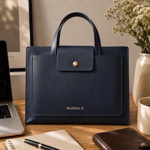 Peut inclure: Un sac à main bleu marine structuré avec deux poignées supérieures et une poche frontale à rabat fermée par un bouton-pression doré. Le nom MARISA K. est imprimé en lettres dorées sur le bas du sac, qui présente une finition lisse.